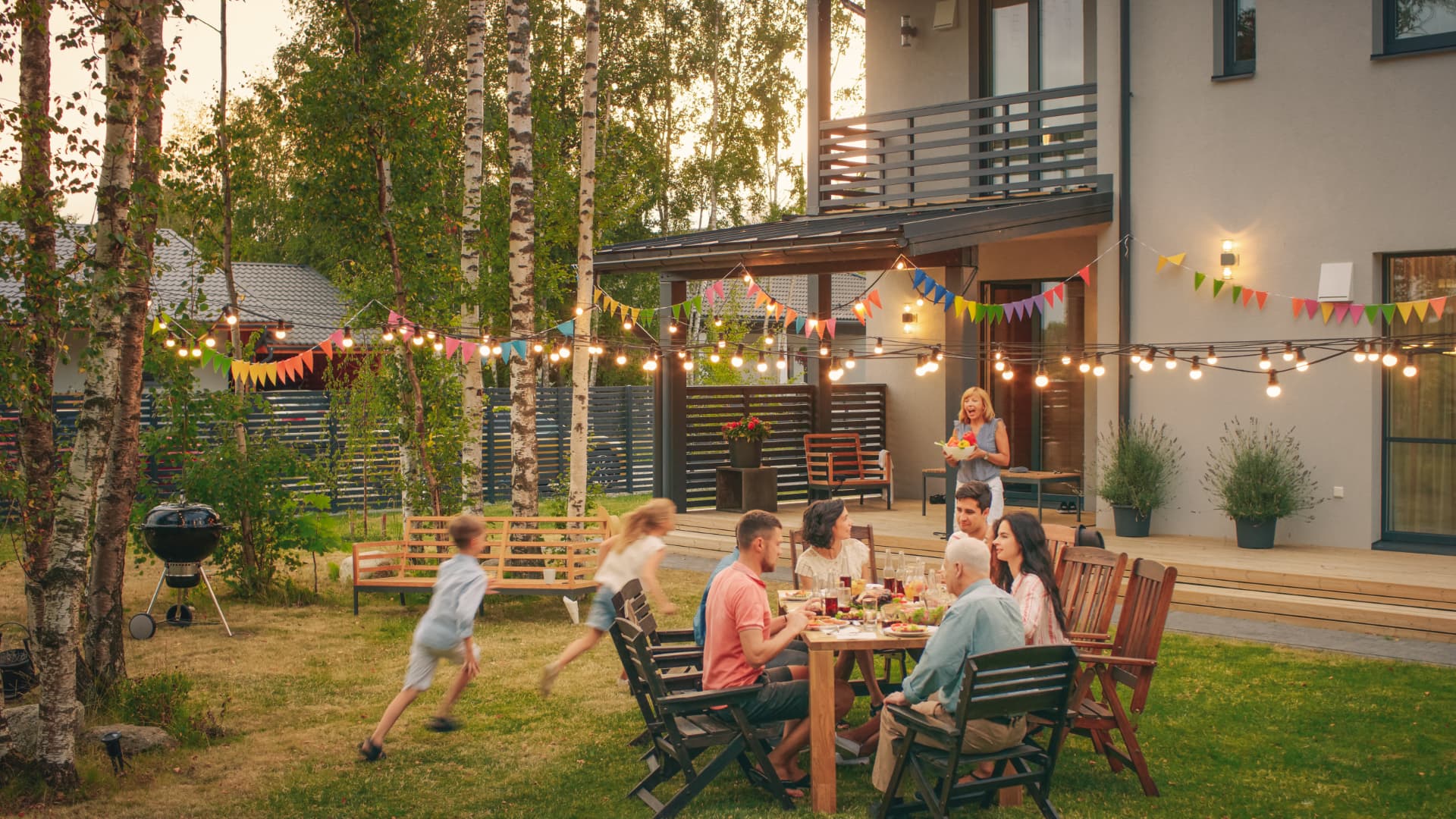 A family eating together under festoon lights in a summer back garden
