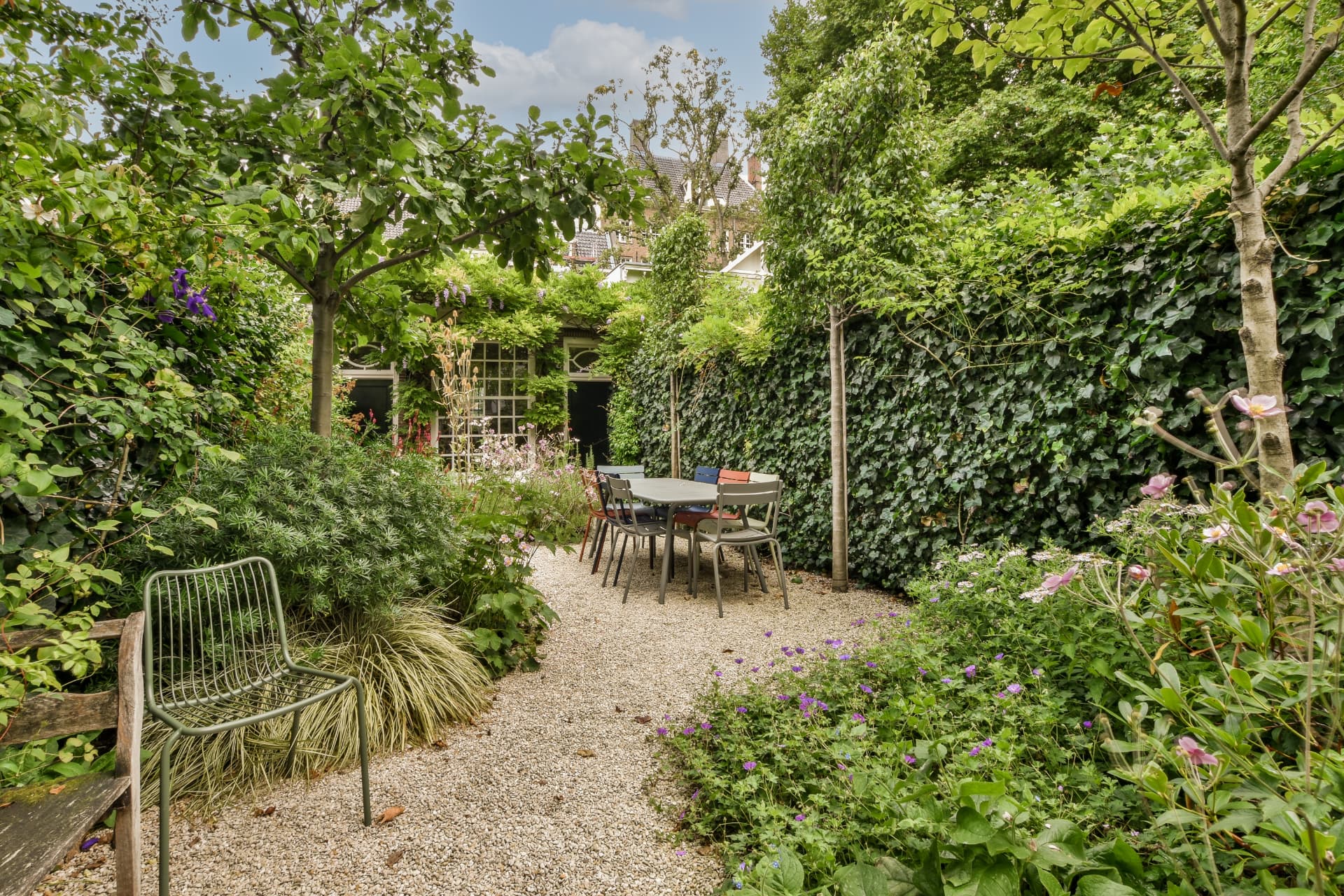 A gravel courtyard dining area framed by clipped ivy hedging, pleached trees and Japanese anemones